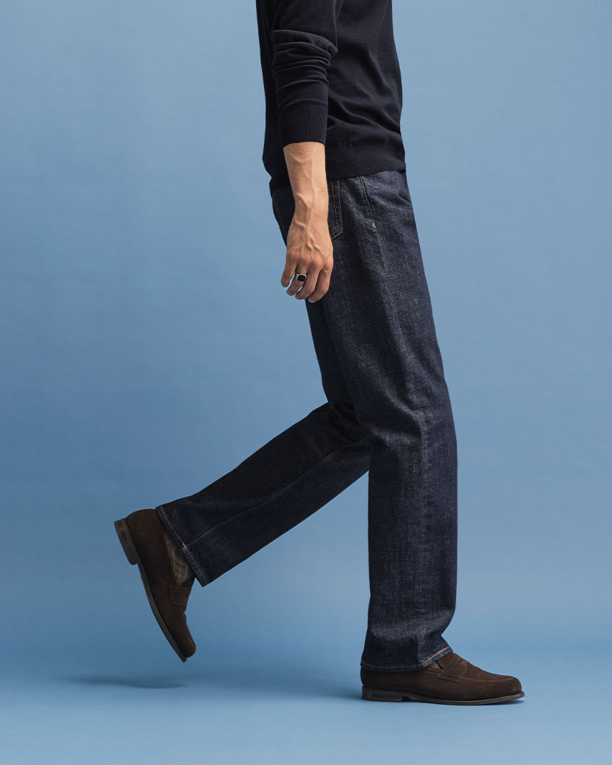 Person i jeans och mörk tröja går mot höger på blå bakgrund.