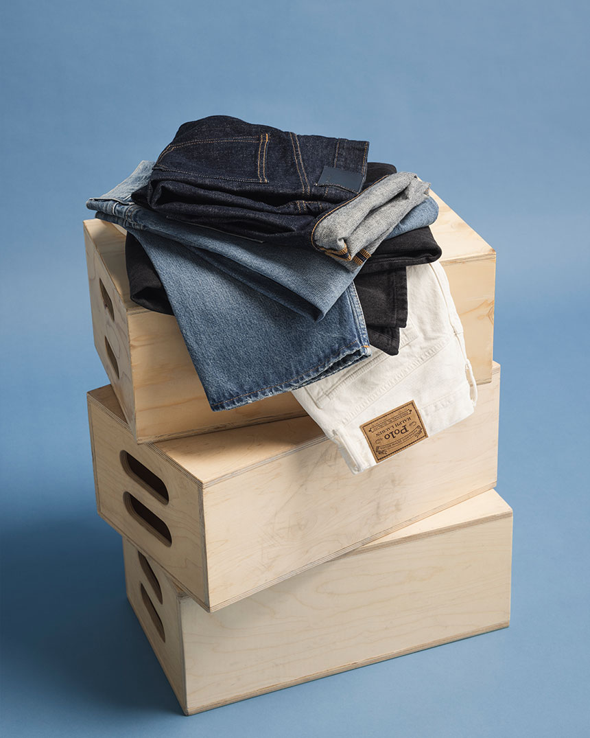 En stapel av vikta jeans ligger på tre träboxar mot en blå bakgrund.