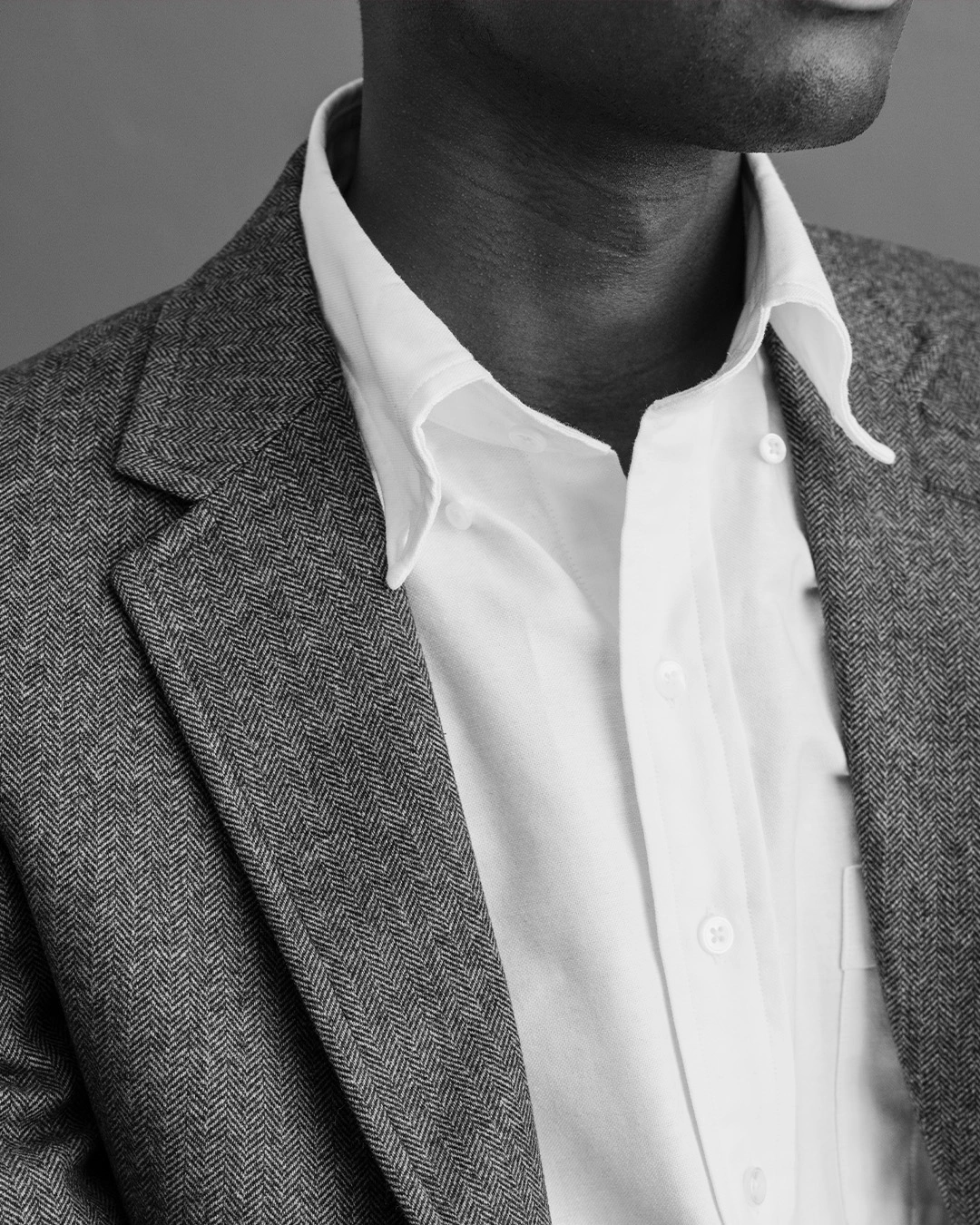 Svartvit närbild på man i vit oxfordskjorta med button down-krage och grå tweedkavaj